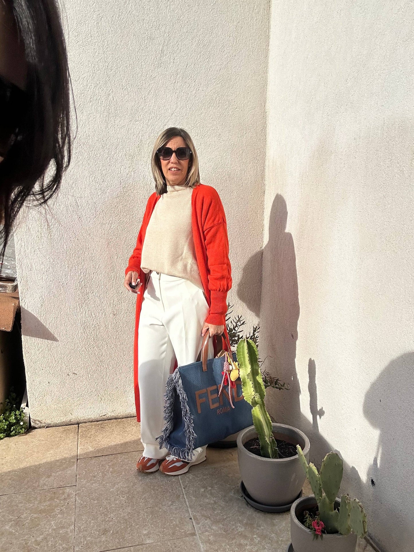 Gilet Olivia orange long et sans boutons, porté avec un sac en jean et un pantalon blanc. Élégance décontractée pour un look moderne et lumineux.