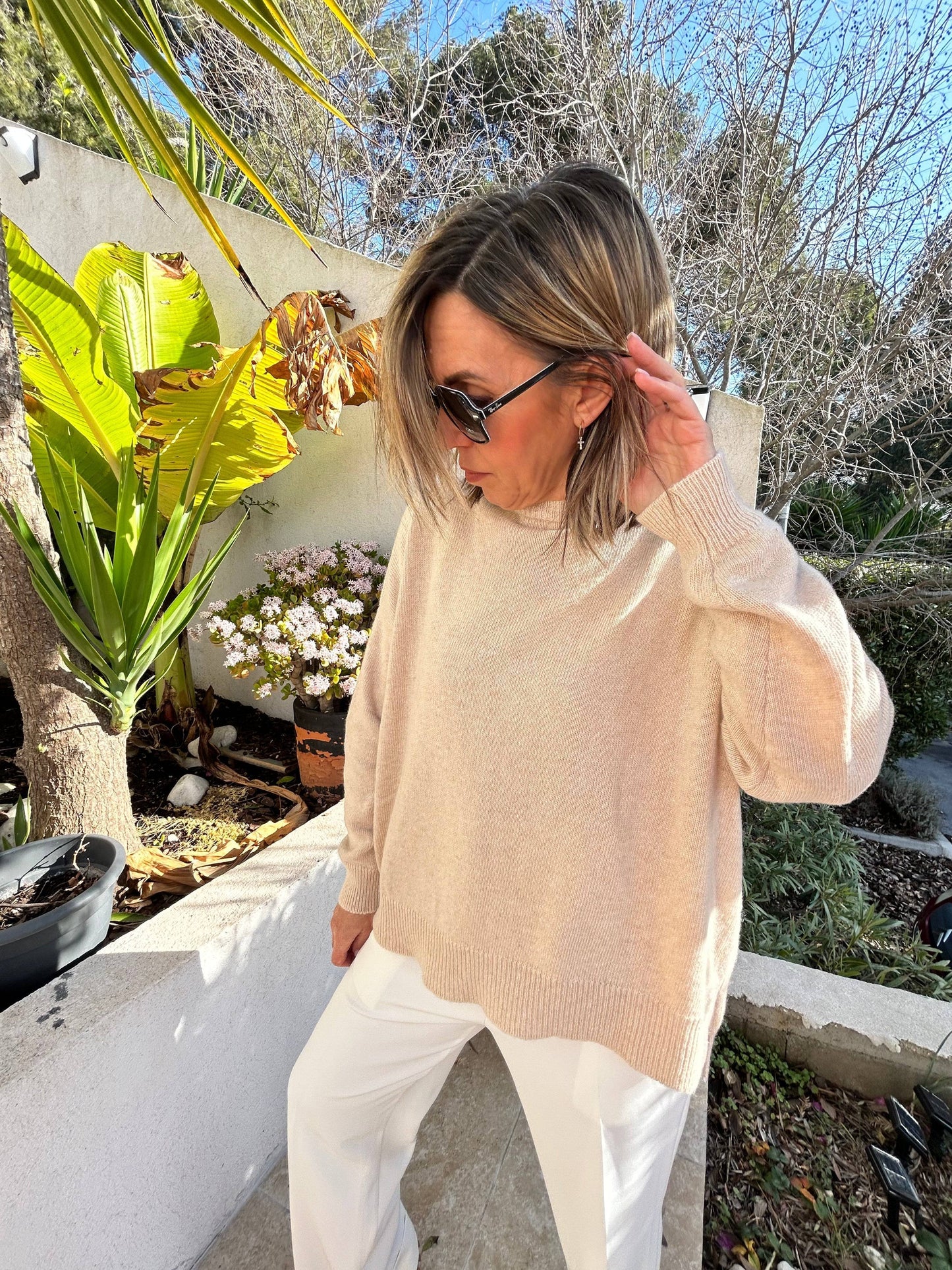 Pull Léa en maille fine beige, col rond, en laine et cachemire, porté avec un pantalon blanc. Confort et élégance pour toutes saisons.