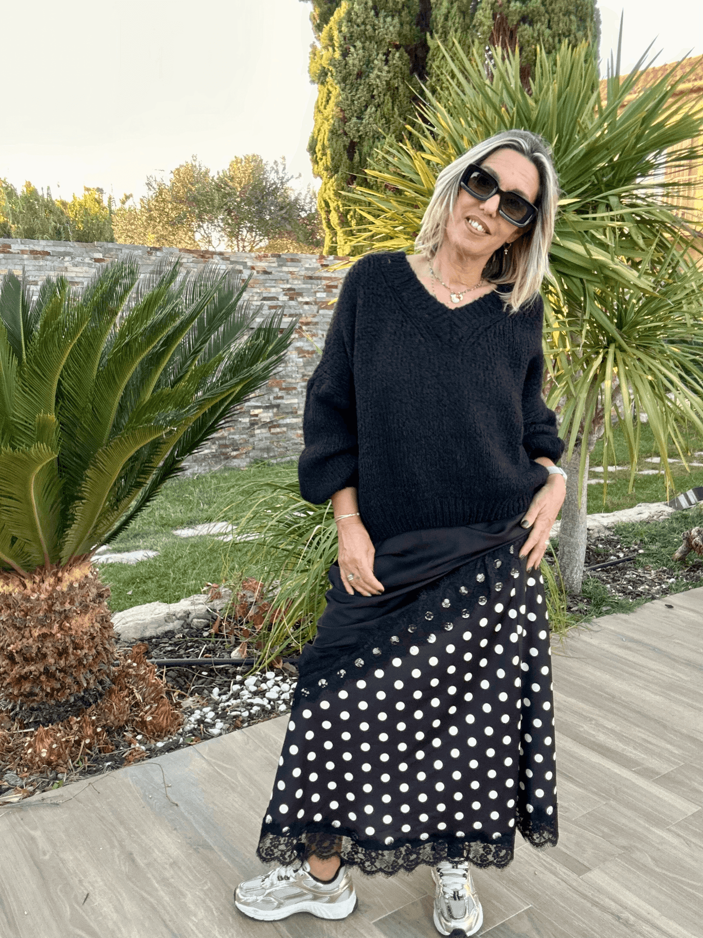 Pull noir Gabriel col V femme en maille chaude, porté avec une jupe à pois et baskets, style tendance 2025 pour un look casual chic.