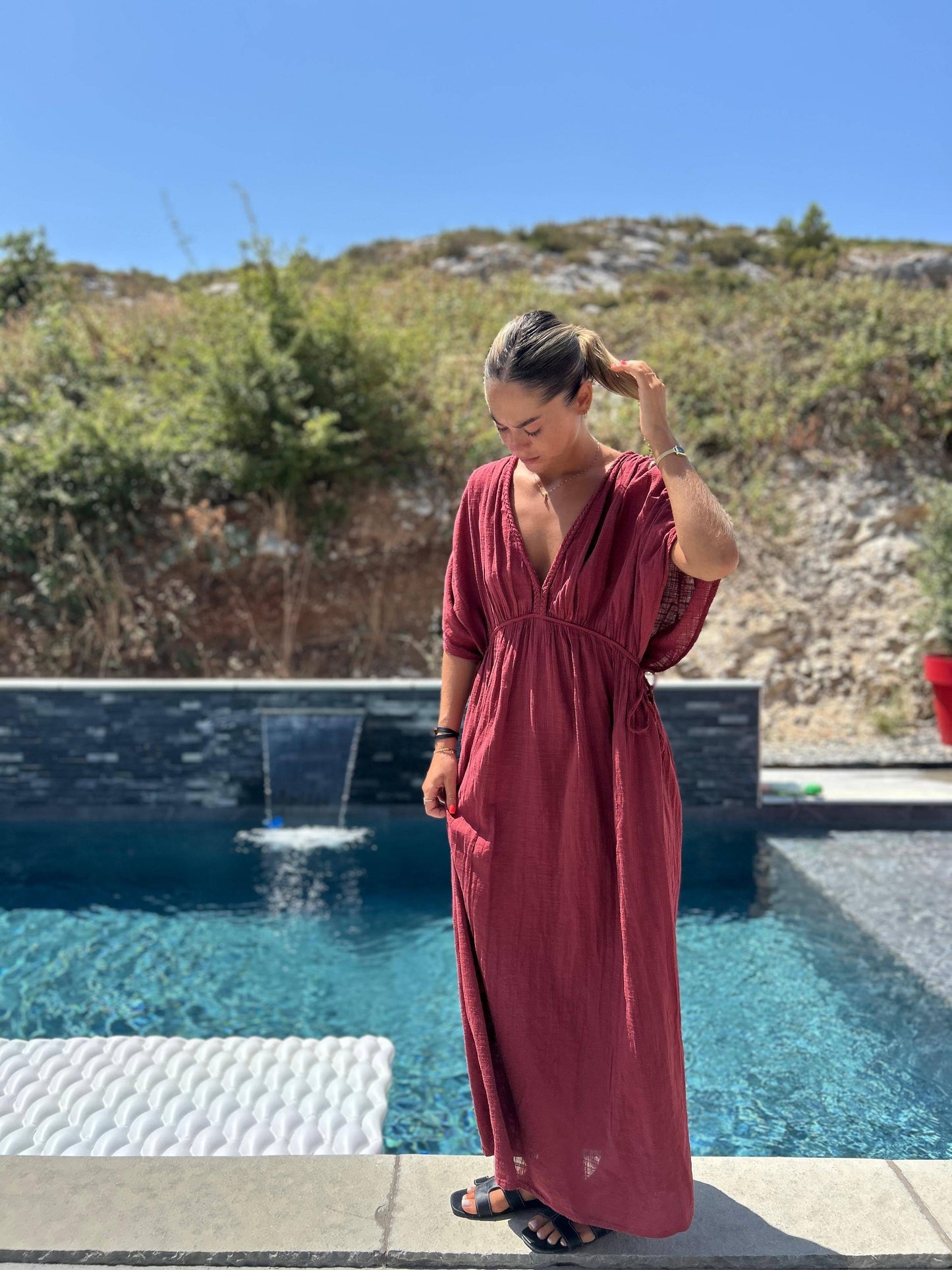 Robe Amaya - Johanna Paris en coton brique, coupe fluide et taille unique, portée au bord d'une piscine, idéale pour l'été 2025.