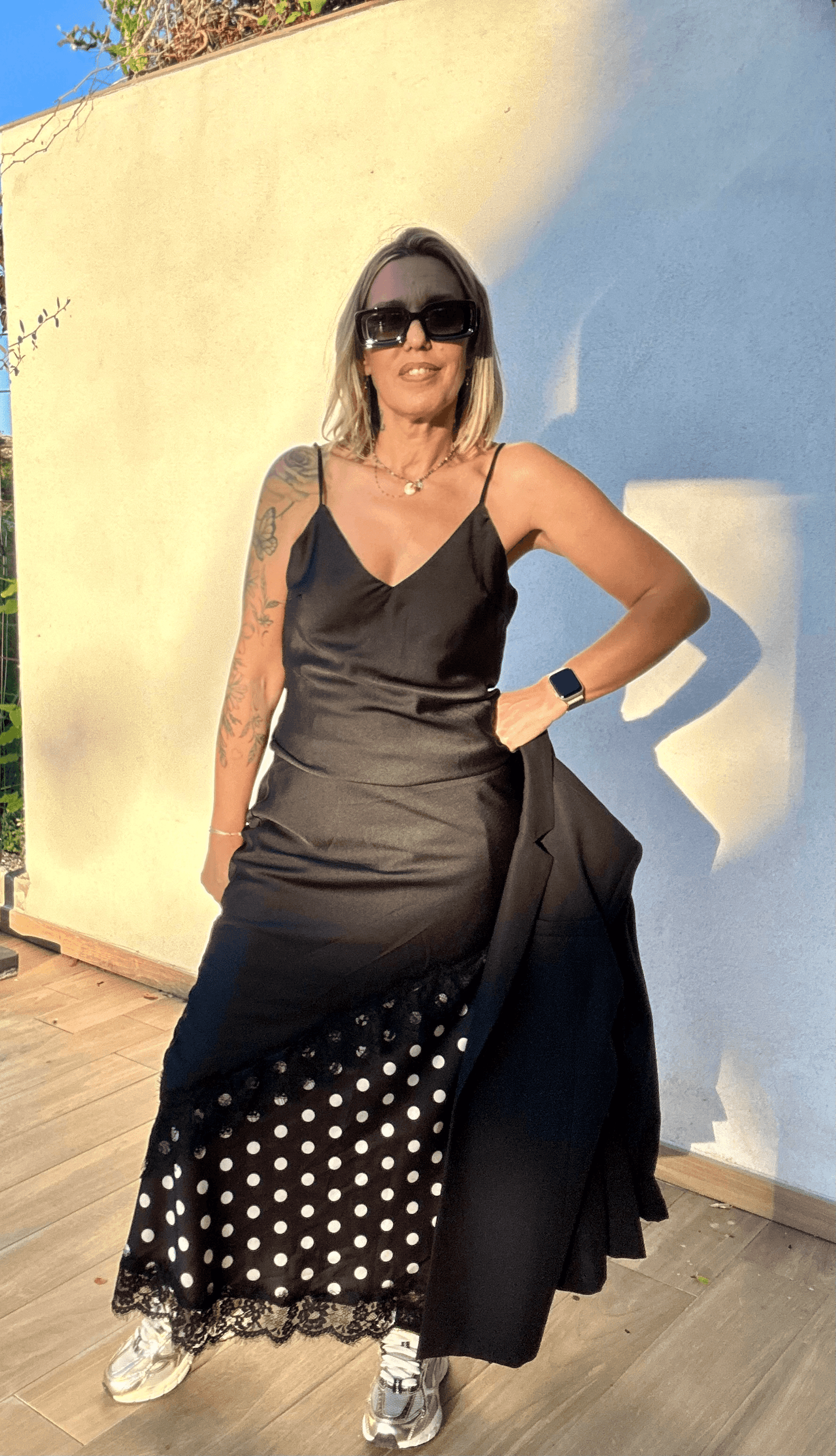 Robe noire asymétrique Carmen avec détails en dentelle et jupe à pois, look chic décontracté avec baskets pour femme moderne.