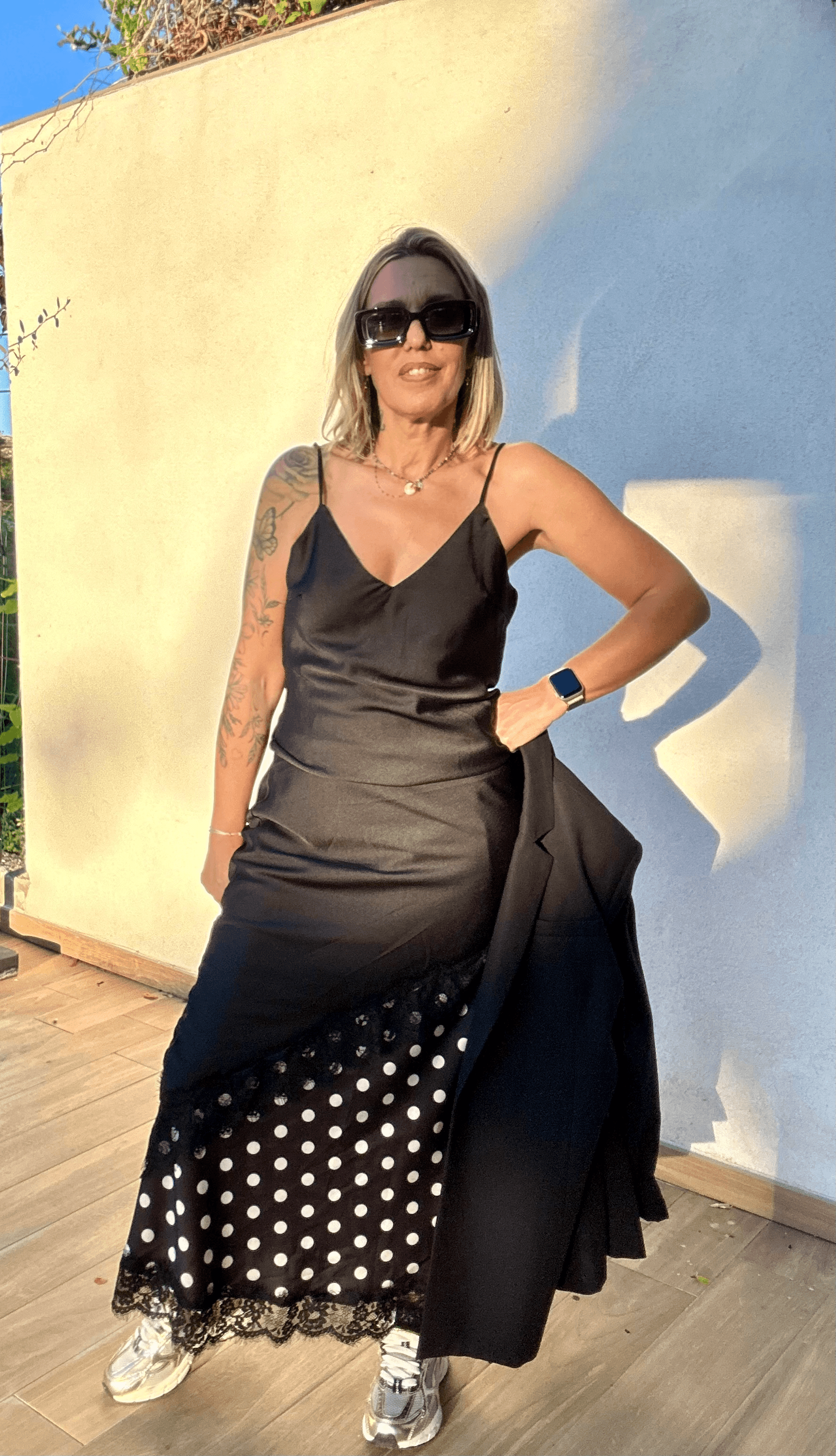 Robe noire asymétrique Carmen avec détails en dentelle et jupe à pois, look chic décontracté avec baskets pour femme moderne.