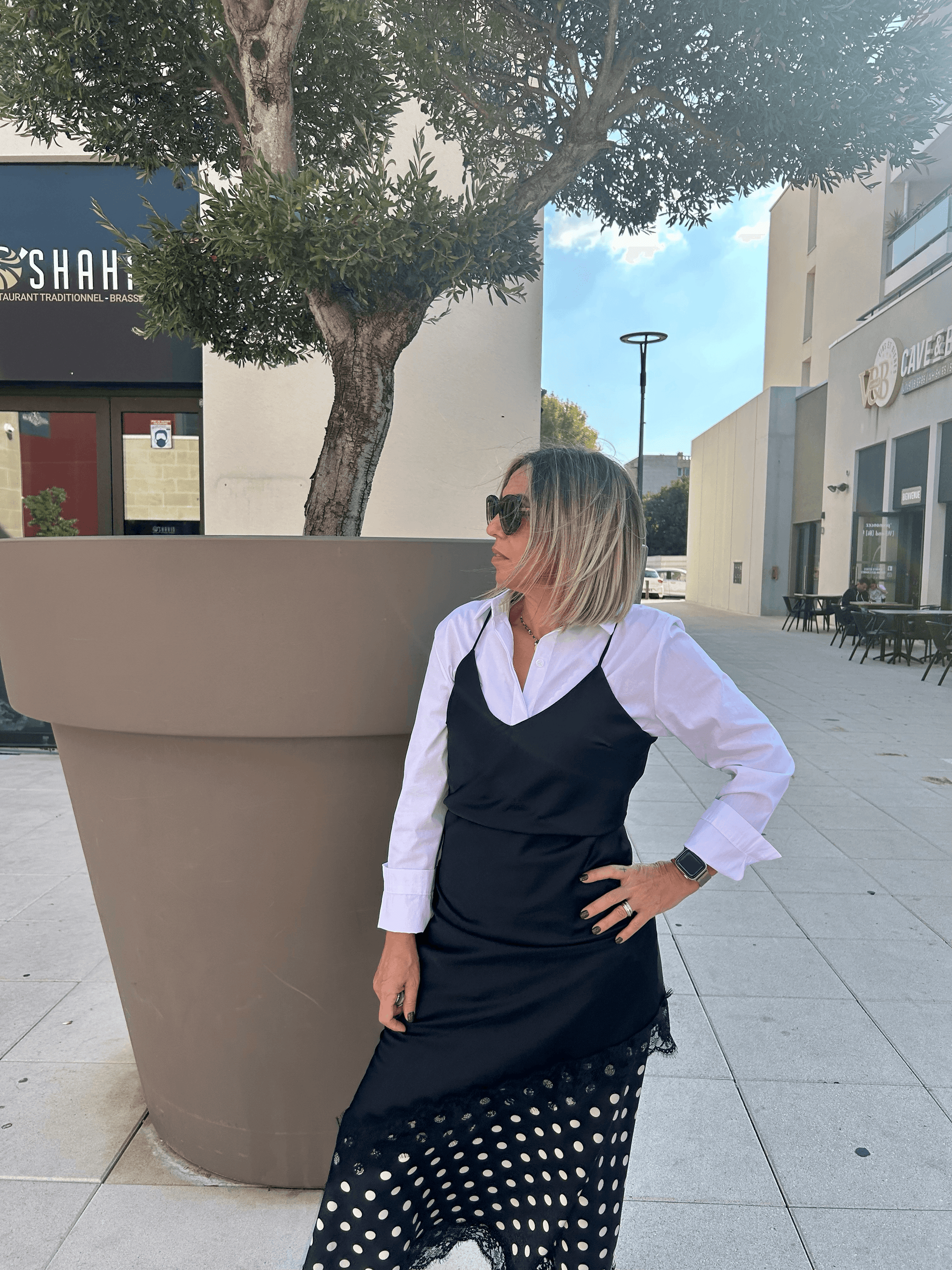 Robe nuisette noire Carmen portée sur une chemise blanche et jupe à pois, style contrasté et raffiné pour une tenue habillée féminine.