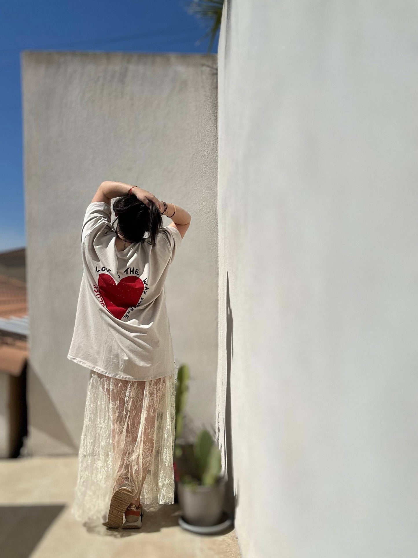 Robe T-Shirt Oversize beige imprimé cœur rouge au dos, associée à une jupe en dentelle, style casual chic femme, collection été 2025.