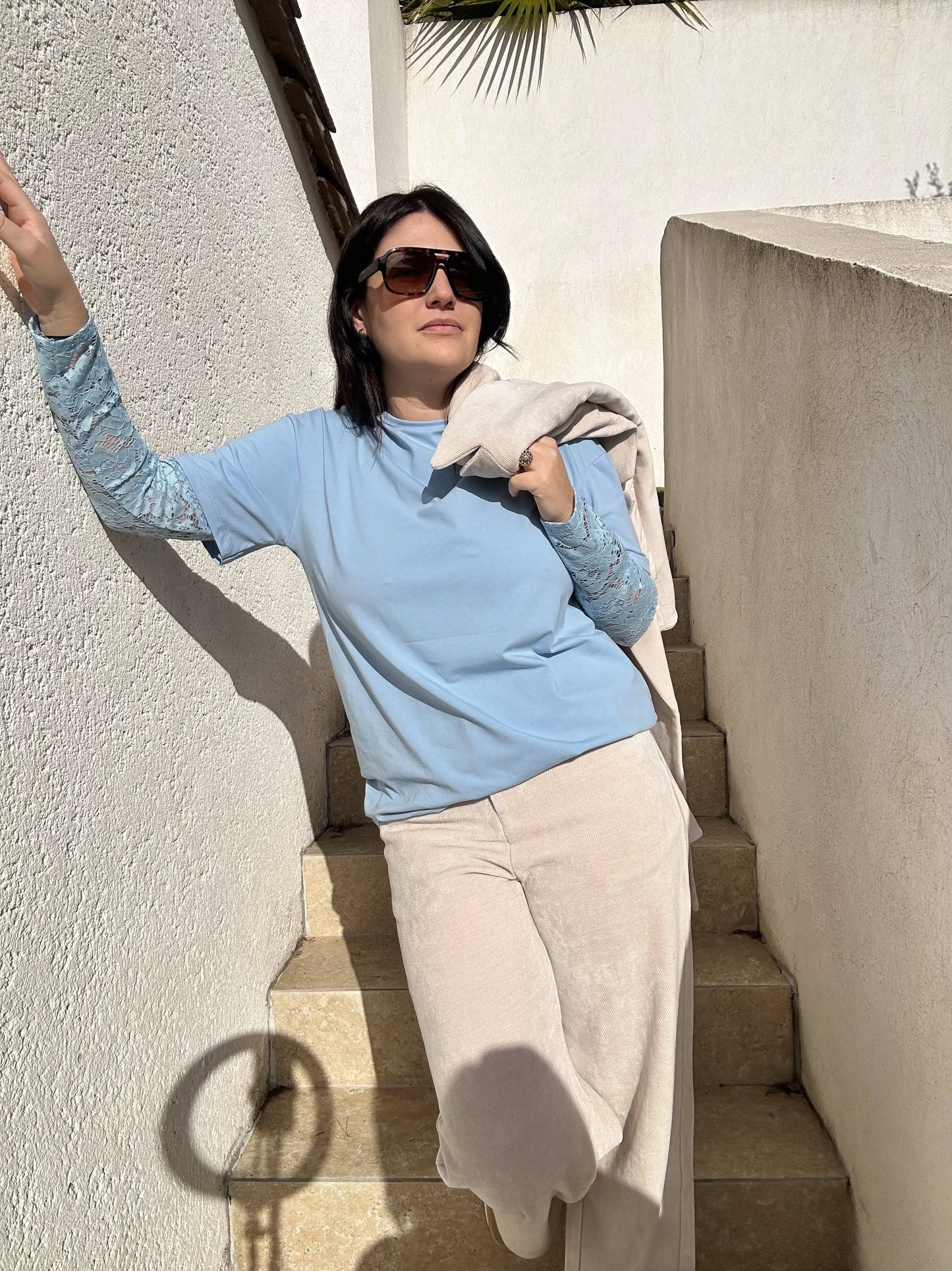 Pantalon Aurélie en velours souple beige, coupe large et taille haute, porté avec un t-shirt bleu et un sous-pull imprimé, style décontracté.