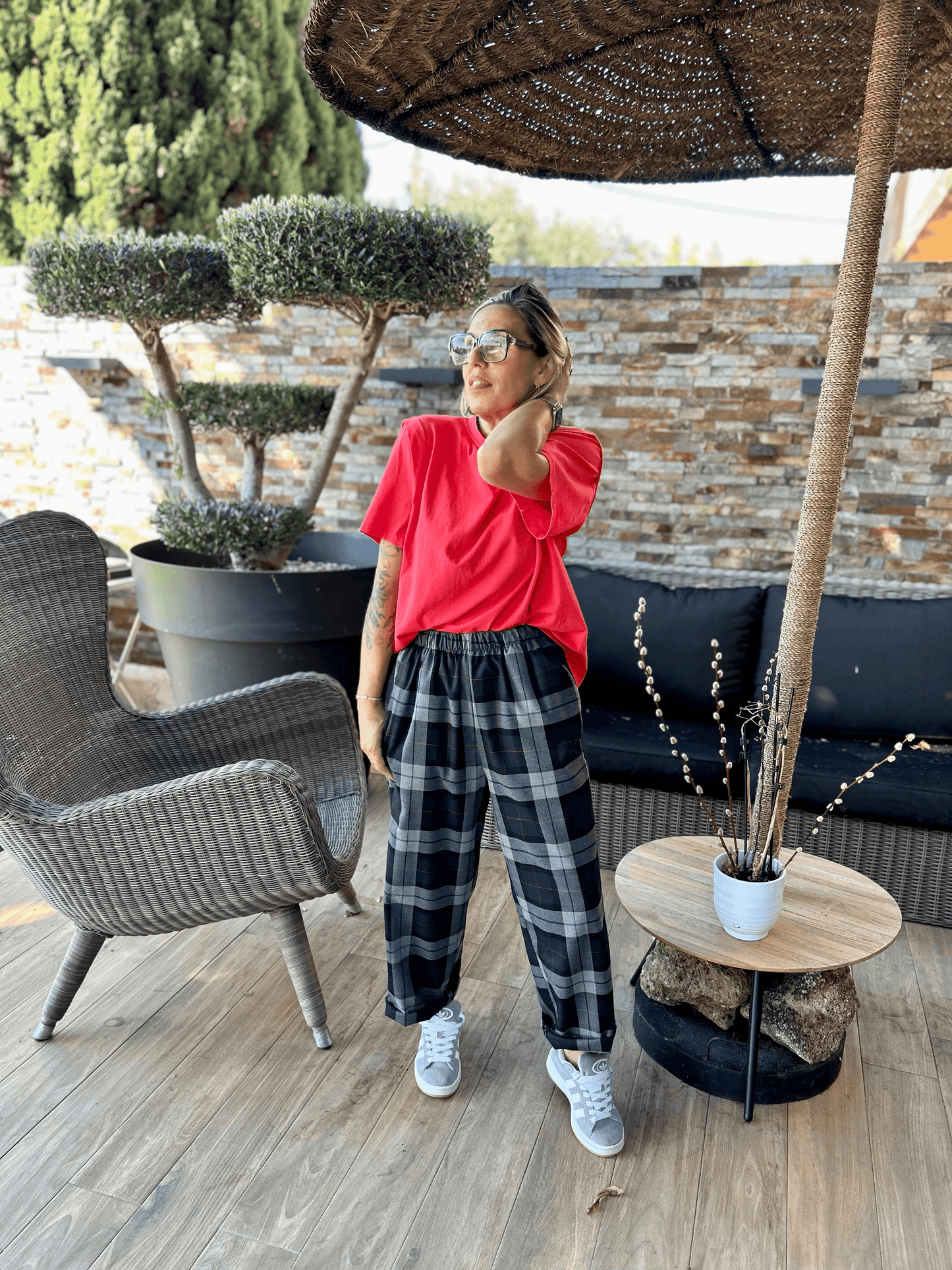 T-shirt Rouge Ella porté avec un pantalon à carreaux noir et blanc, look décontracté chic en extérieur sous une pergola en rotin.
