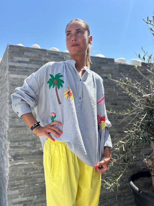 Blouse Paloma by Johanna Paris à rayures bleues avec broderies colorées, portée avec un pantalon jaune, style bohème chic pour l'été.