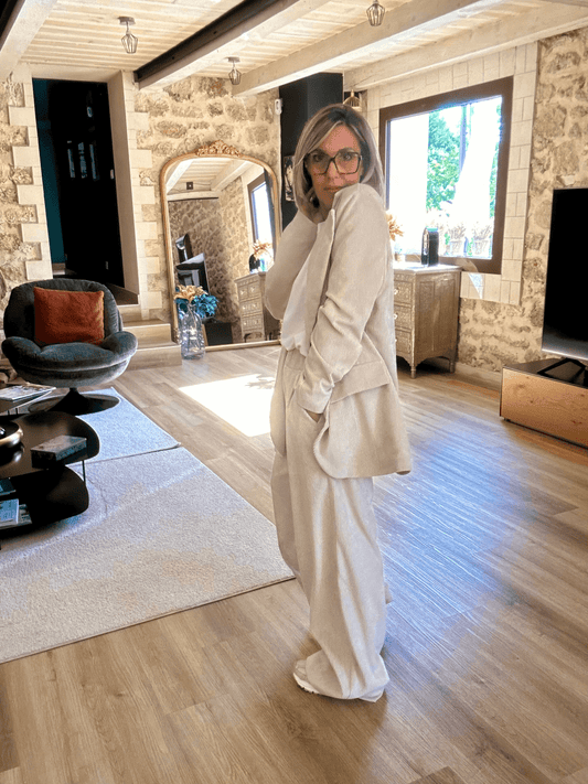 Pantalon Amara en velours beige à taille élastique, coupe large et fluide, porté en intérieur avec un blazer assorti pour un look chic décontracté.