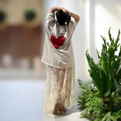 Jupe Diva Boho Chic Lace Maxi Skirt écrue portée avec un t-shirt oversize à motif cœur, style bohème décontracté pour l'été 2025.