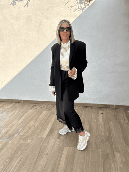 Jupe noire satinée femme Ziggy avec bord dentelle, portée avec un blazer noir oversize et des baskets, tenue chic et moderne automne-hiver 2025.