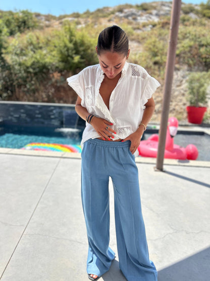 Pantalon Céleste Johanna Paris fluide bleu clair, coupe large et taille élastique, porté en extérieur avec chemisier blanc pour un look d'été chic.