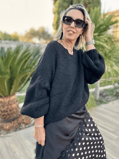Pull noir col V Gabriel porté avec une jupe noire à pois blancs, idéal pour un look automne chic et décontracté. Maille douce et manches bouffantes.