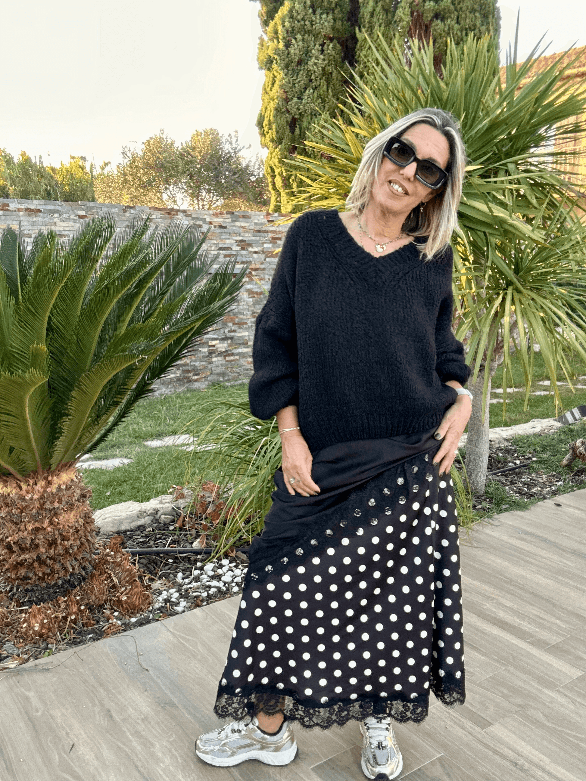 Pull noir Gabriel col V femme en maille chaude, porté avec une jupe à pois et baskets, style tendance 2025 pour un look casual chic.