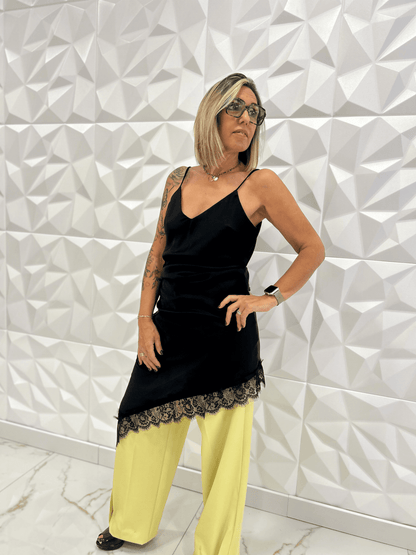 Robe nuisette noire asymétrique Carmen portée avec un pantalon jaune large, dentelle fine en bas, style chic et moderne pour femme tendance 2025.