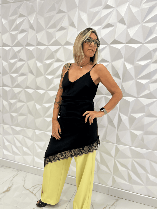 Robe nuisette noire asymétrique Carmen portée avec un pantalon jaune large, dentelle fine en bas, style chic et moderne pour femme tendance 2025.