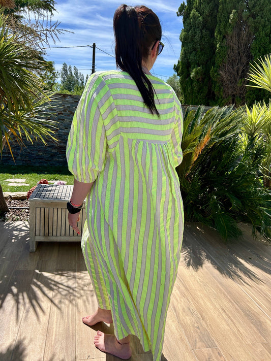 Robe Ibiza longue bohème chic à rayures fluo jaune, coupe oversize en coton, portée en extérieur dans un jardin ensoleillé.