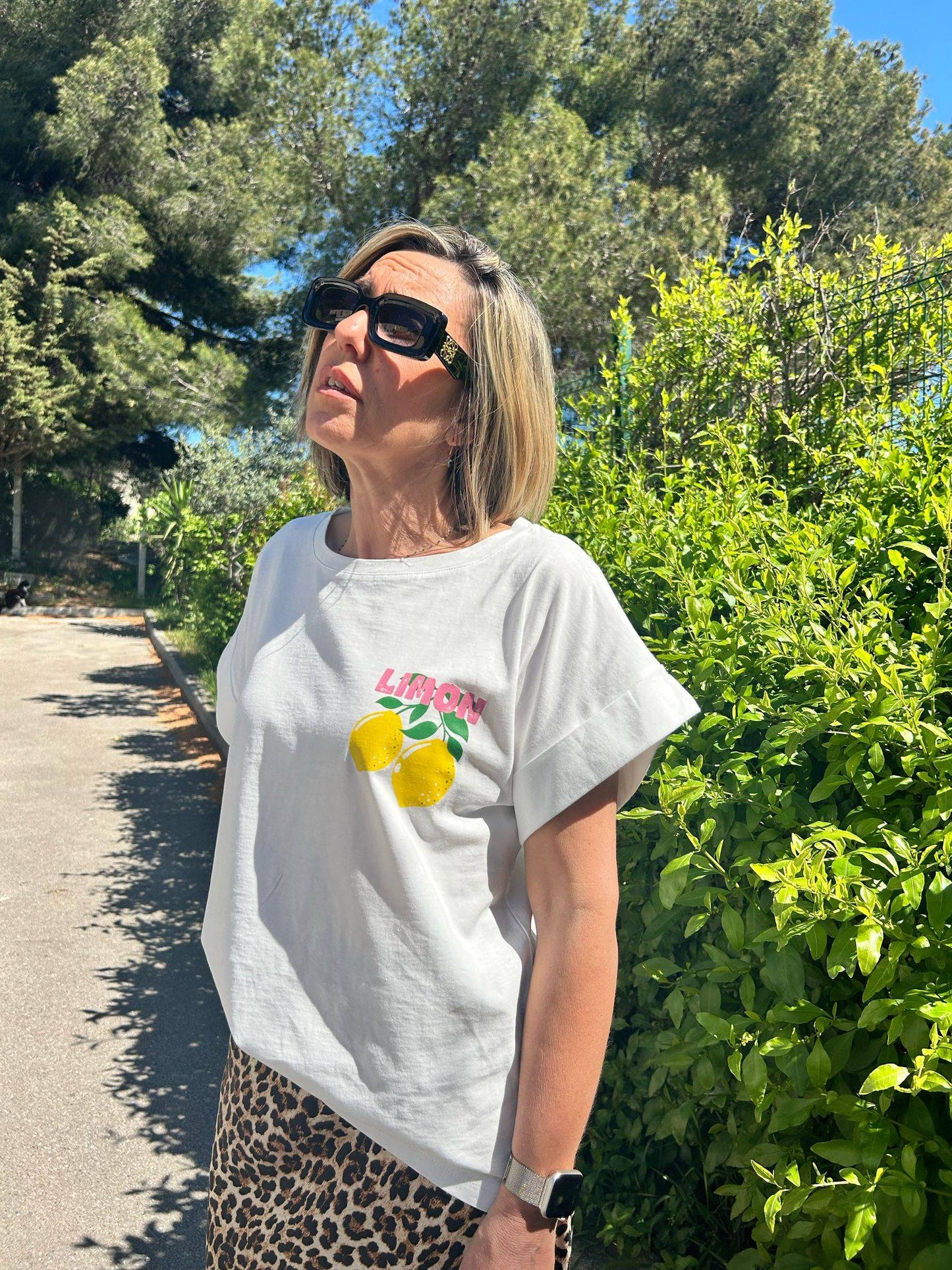 T-shirt Limoncello parfait pour l'été 2025, coupe droite en coton blanc avec motif citron, porté avec une jupe léopard sous le soleil.