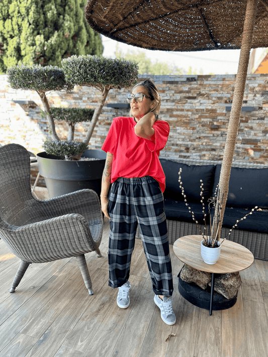 T-shirt Rouge Ella porté avec un pantalon à carreaux noir et blanc, look décontracté chic en extérieur sous une pergola en rotin.